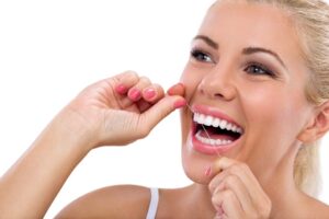 Woman flossing her teeth at dentist in Inwood Village.