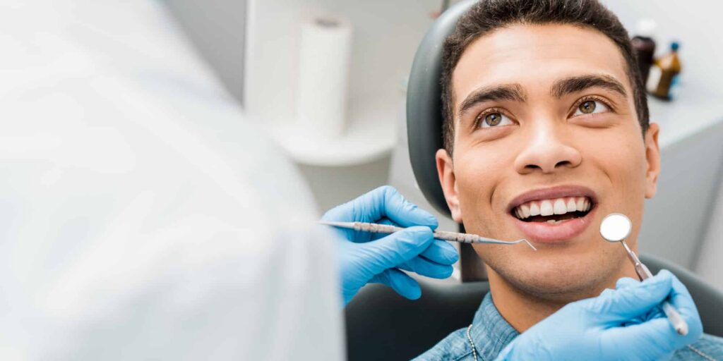 man smiling during a dental exam with a dentist holding a mirror and dental tool at Inwood Village Dental in Dallas, TX